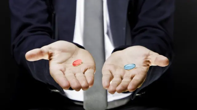 Мужчина держит на ладонях две таблетки - красную и синюю.