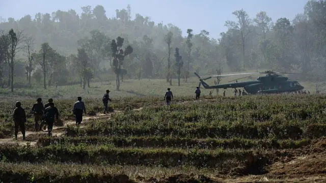 စစ်ရဟတ်ယာဥ်တစ်စင်းဆီ သွားနေတဲ့ မြန်မာစစ်တပ်တပ်ဖွဲ့ဝင်တွေ။ တောင်ပေါ်ဒေသမှာဖြစ်ပြီး လယ်ကွက်တစ်ခုကို ဖြတ်သွားနေတာဖြစ်ပါတယ်။