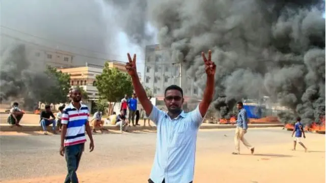 One protester makes the victory sign against a backdrop of burning tyres