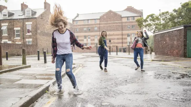 Meninas pulam e sorriem na rua sob chuva