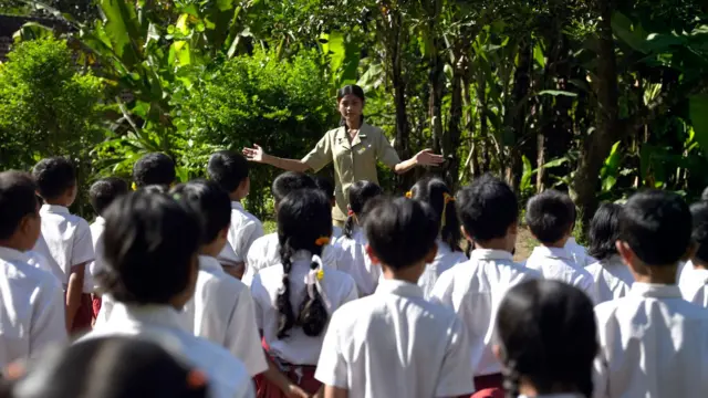 Seorang guru di sekolah dasar sedang memberikan arahan kepada murid-muridnya. 