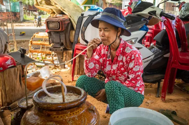 Một người phụ nữ ngồi xổm uống rượu cần ở Kon Tum