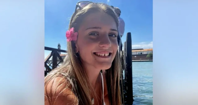 Saçlarında çiçek olan bir kız kameraya bakarak gülüyor.