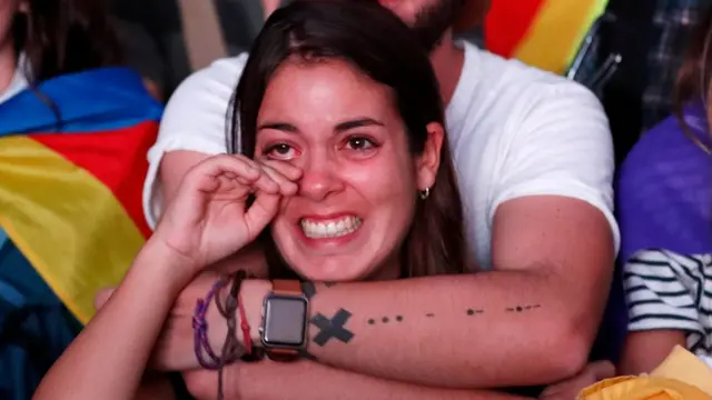 Una joven llora mientras ve la comparecencia de Puigdemont en una pantalla gigante en la calle.