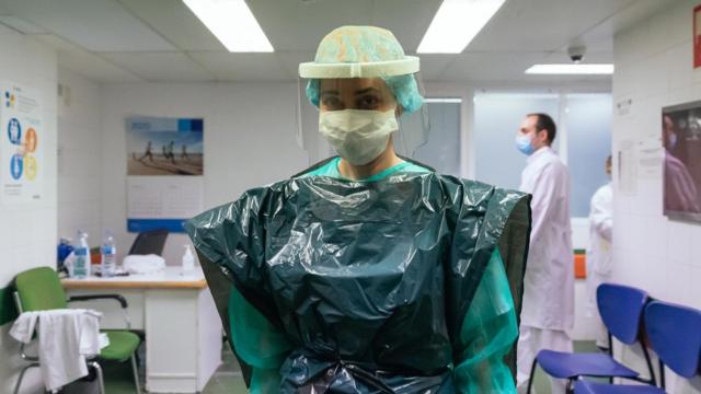 Além do EPI, uma enfermeira de terapia intensiva na Espanha usa um saco de lixo e uma máscara plástica protetora, doada por uma empresa local.