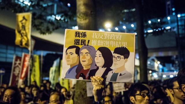 示威者拿着牌子，抗议香港当局取消四名非建制派议员的资格