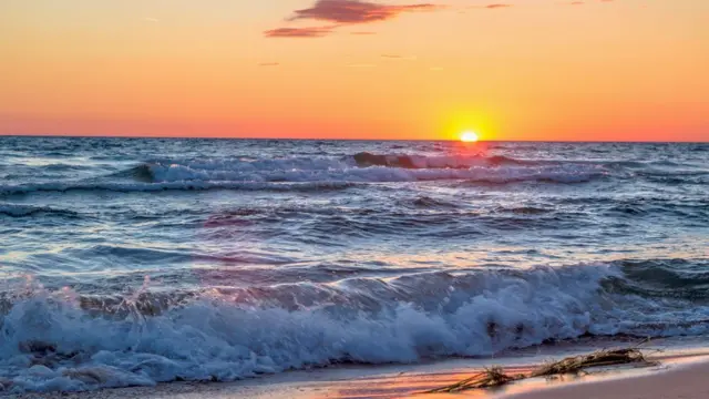 Imagem mostra o mar, com o sol se pondo, ao fundo