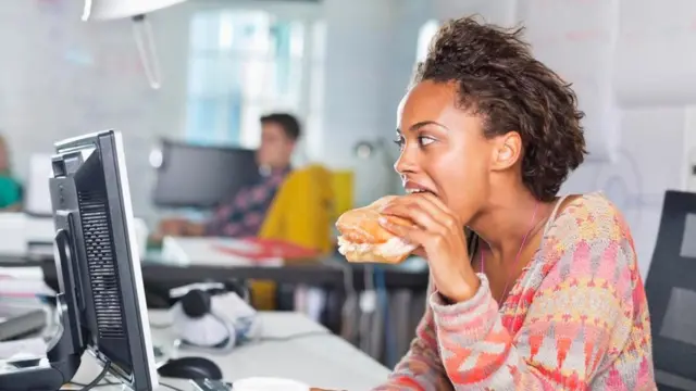 موظفة تتناول الطعام وهي تجلس على مكتبها