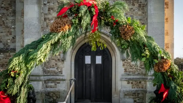 Украшенные еловыми ветками и красными лентами ворота сельской церкви