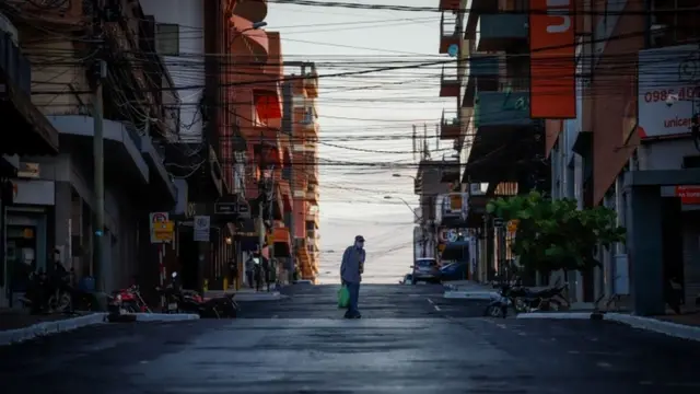 Homem atravessa rua vazia, rodeada de prédios