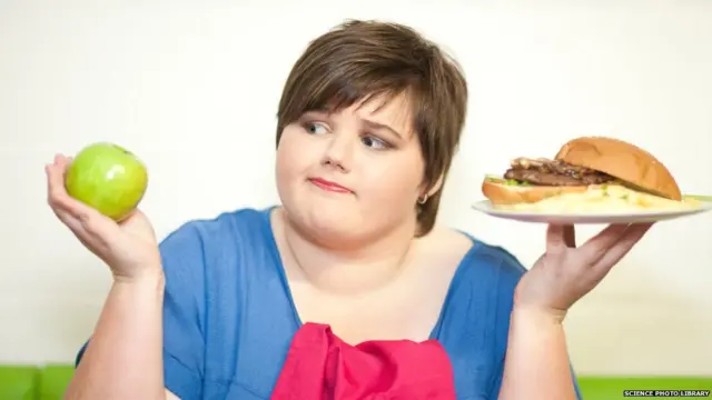 Young woman choosing between an apple and a burger.