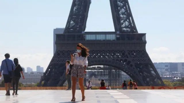 A woman in a face mask walks in front of the Eiffel Tower in Paris