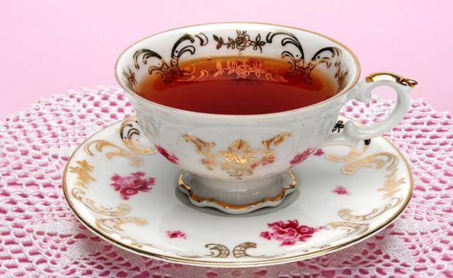 Du thé dans une tasse en porcelaine, avec des décorations dorées et des roses peintes dessus.