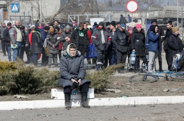 People wait in a long queue during the distribution of humanitarian aid near a damaged store of wholesaler Metro in the course of Ukraine-Russia conflict in the besieged southern port city of Mariupol, Ukraine March 24, 2022.