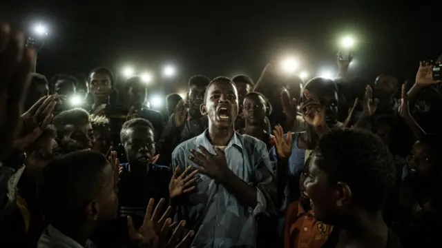 Un joven, iluminado por teléfonos móviles, recita un poema mientras los manifestantes cantan consignas pidiendo un gobierno civil, durante un apagón en Jartum (Sudán), el 19 de junio de 2019.