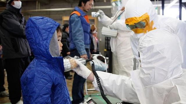คนงานตรวจหาสารกัมมันตรังสีจากเด็กชายคนหนึ่ง ใกล้กับโรงไฟฟ้าฟุกุชิมะ มี.ค. 2011