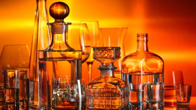 Various glass containers with alcohol against an orange-red background