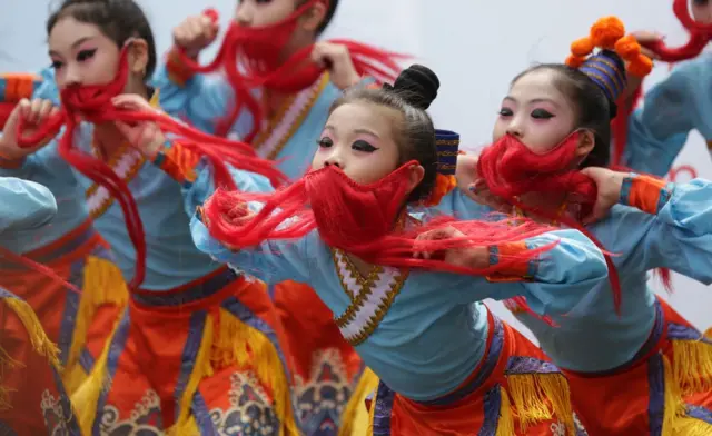 A row of dancers perform with colourful hair over their faces on The Royal Mile in Edinburgh as part of an Edinburgh Fringe Festival.