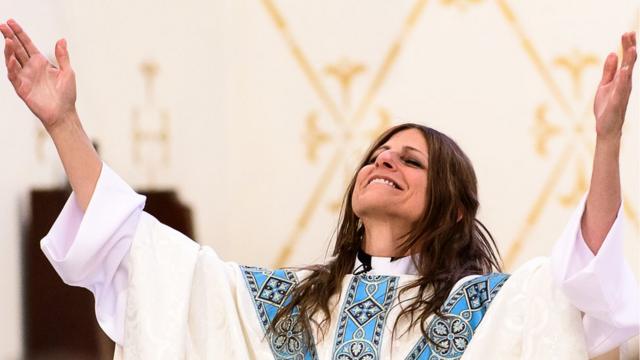 Fotografia colorida mostra mulher brancacomo jogar loterias caixa onlinecabelo comprido sorrindo com as mãos para o alto e usando roupascomo jogar loterias caixa onlinepadre