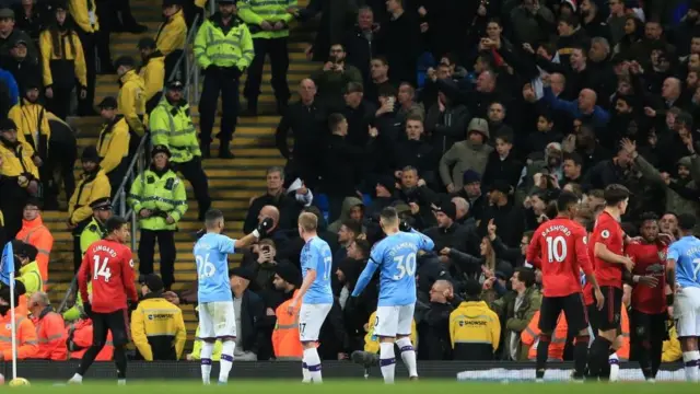 Les joueurs de Manchester City interviennent auprès des supporters de la ville qui raillent et lancent des objets sur les joueurs de Manchester United