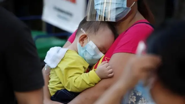 A shopper holding a baby stands next to makeshift stores selling items at bargain price along a road in Manila, Philippines, 23 December 2020