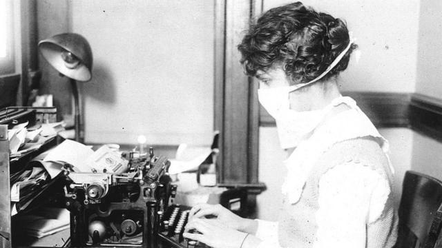 Una secretaria con mascarilla escribe a máquina en su escritorio en 1918