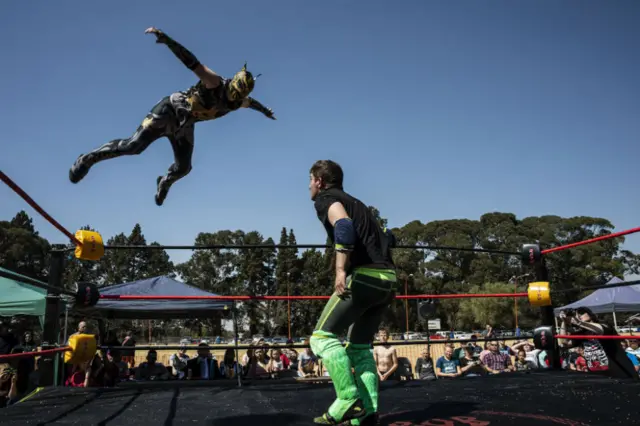 A masked wrestler leaps at his opponent from the corner of the ring.