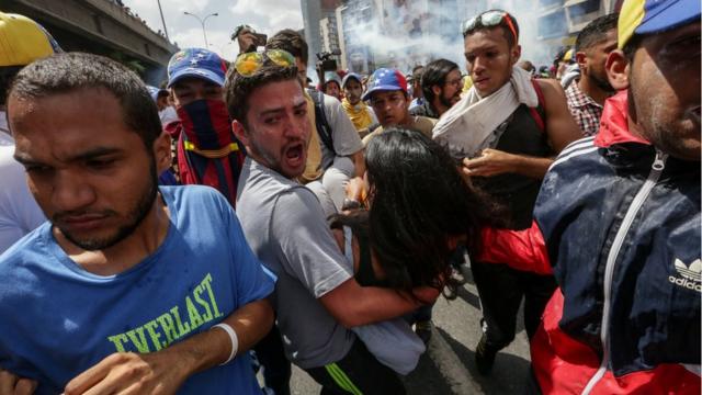 Varios manifestantes llevan cargada a una mujer en medio de las protestas.