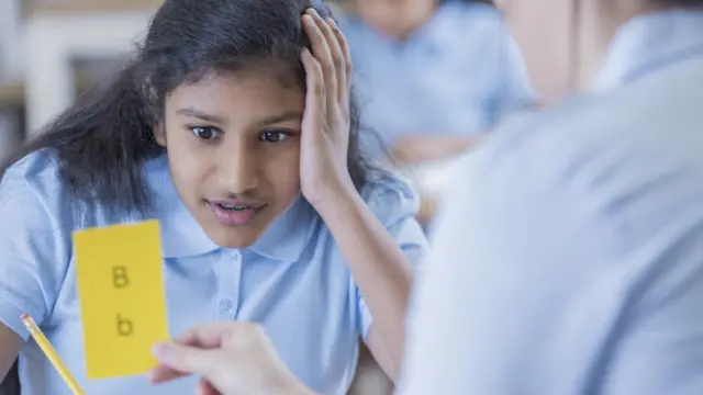 Una niña intenta leer con dificultad una tarjeta con las letras "b" en minúscula y mayúscula.