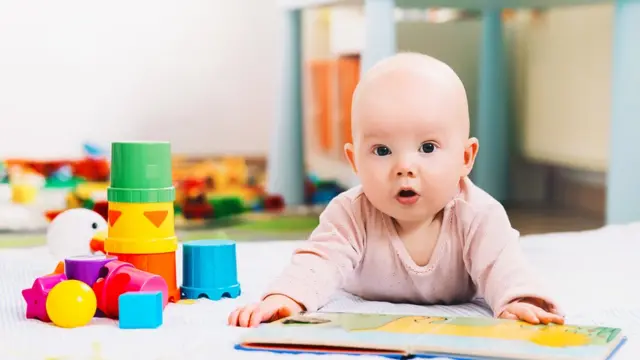 Bebé con un libro y juguetes.