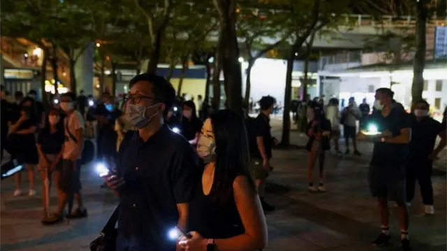 Personas con la luz de sus celulares encendidos cerca del parque Victoria de Hong Kong.