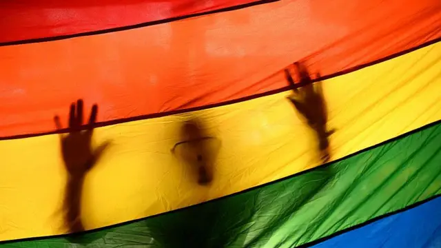 An outline of a man is seen behind a rainbow LGBTQ+ flag at a march. Stock photo from library, not taken in Senegal.