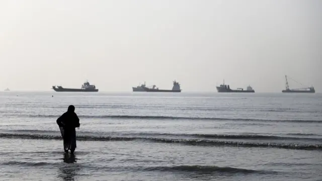 Una mujer en una playa de Irán frente a varios buques en el estrecho de Ormuz