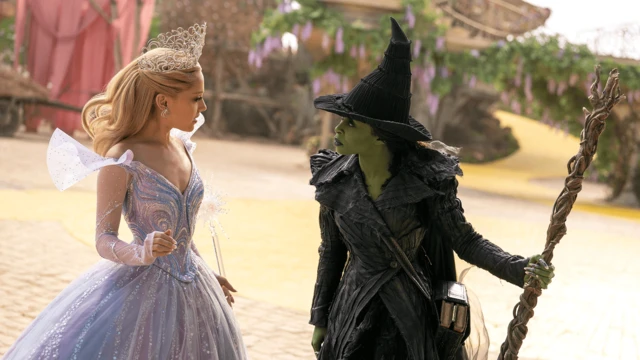 Escena de "Wicked", con Ariana Grande con un vestido de princesa y una corona, y Cynthia Erivo con la piel verde vistiendo un traje y sombrero puntiagudo negros.