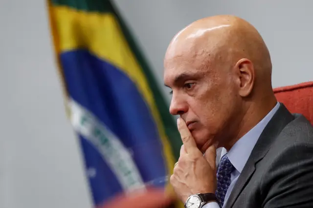 Alexandre de Moraes de perfil, com a mão sobre a boca