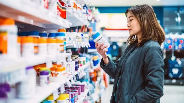 Mulher lendo rótulo de produto na farmácia