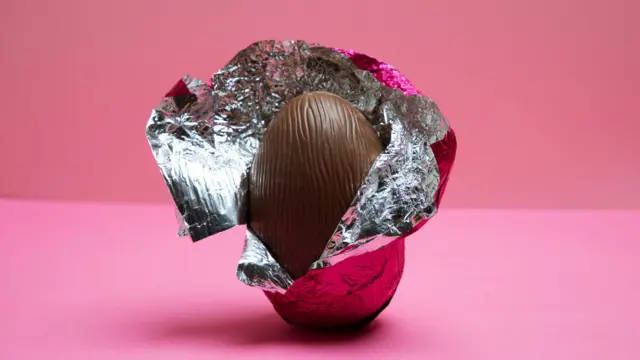 Um ovo de páscoa com embalagem aberta em fundo rosa