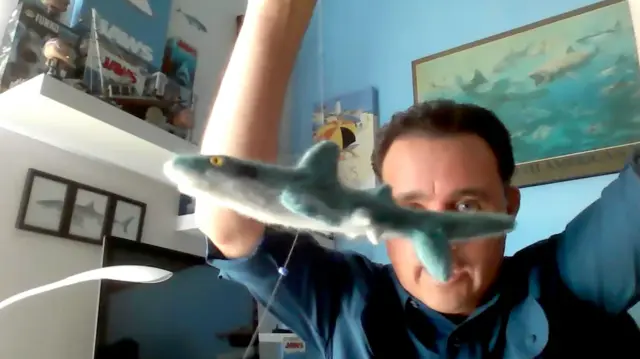 Mauricio Hoyos segura um pequeno tubarão-das-galápagos de brinquedo nas mãos