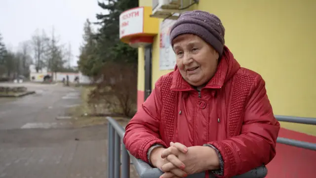 An elderly Belarusian lady wearing a red coat and a purple hat. 