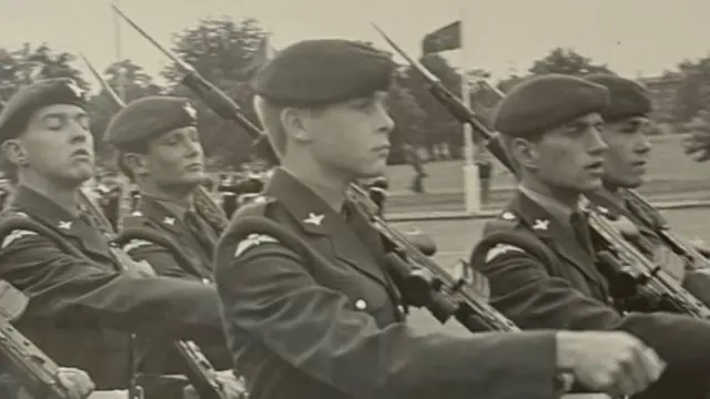 Imagem em preto e branco mostra jovens integrantes do Regimento de Paraquedistas marchando em um pátio de formatura. Os soldados carregam fuzis SA80 com baionetas fixadas