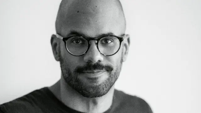 Kauê Lopes dos Santos, um homem careca, de barba curta e óculos, vestindo camiseta escura, em foto de rosto tirada com ângulo fechado