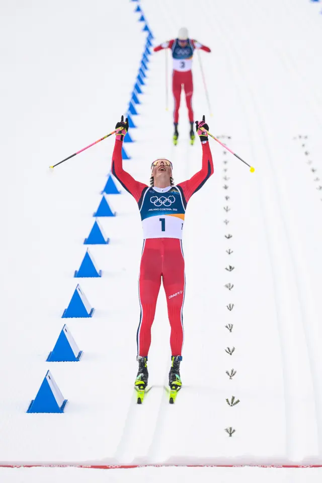 Лыжник с поднятыми руками, в которых палки, празднует победу