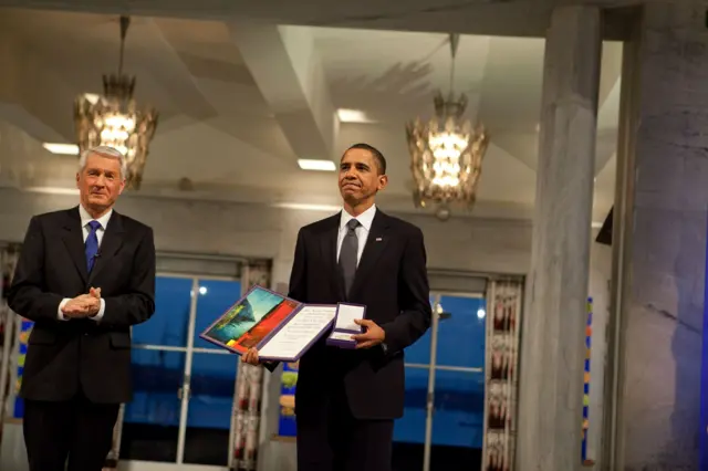 Obama em pé, sorrindo contidamente e segurando diploma