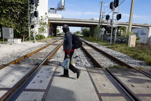 Una persona con gorra y mochila a la espalda cruza las vás del Brightline en Miami. 