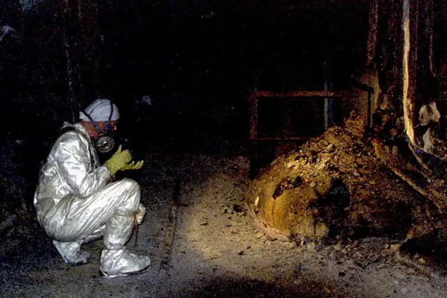 Pesquisador agachado tirando foto da 'pata de elefante', uma formação de cório sob o reator 4 de Chernobyl