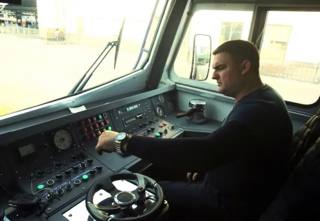 Машиніст потяга керує потягом. Він дивиться на панель управління, нахмуривши брови 