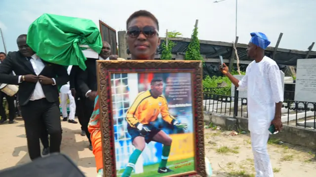 Aworan ọmọbinrin Peter Rufai to gbe aworan oloogbe naa lọwọ ni iboji rẹ to wa ni Ikoyi, niluu Eko