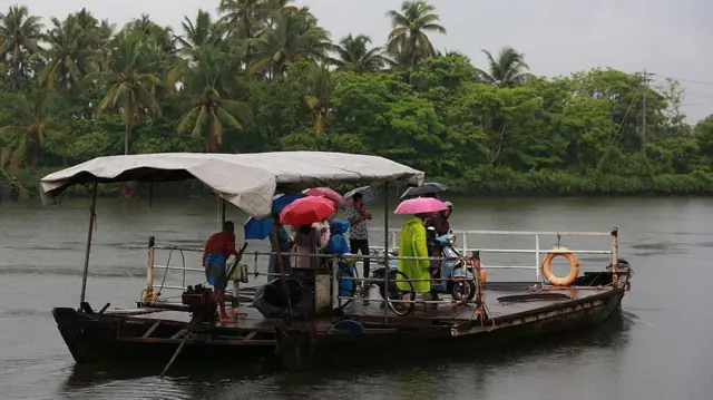 বর্ষার মধ্যে একটি নৌকায় কেরালার কাডামাকুডি গ্রামে পেরিয়ার নদী পার করছেন মানুষ