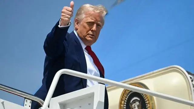 Donald Trump faz sinal de positivo no alto da escada do avião