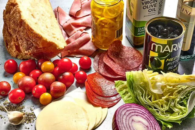 İtalyan Sandviç Salatası Malzemelerinin fotoğrafında domatesler, salam, ekmek, soğan, zeytin, kaşar gibi ürünler estetik bir şekilde fotoğraflanmış